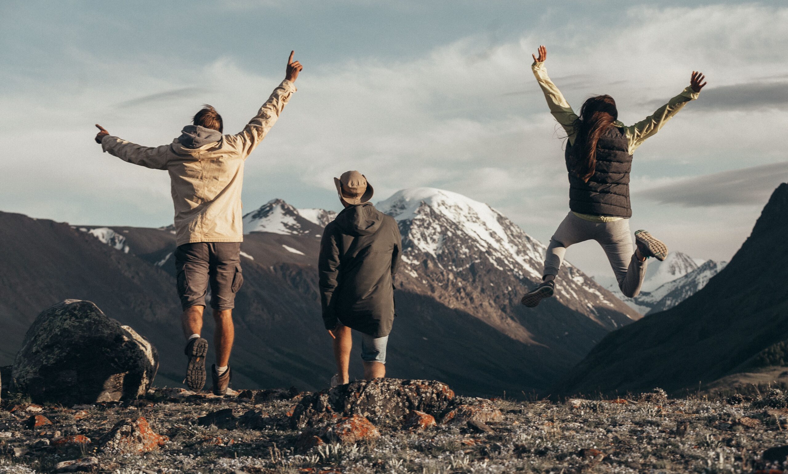 Three people enjoying a hike in snow-capped mountains, jumping with joy filled with adventure.