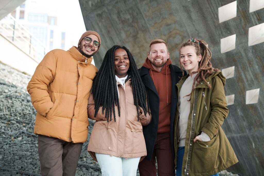 A group of four friends in winter attire smiling outdoors, enjoying togetherness.