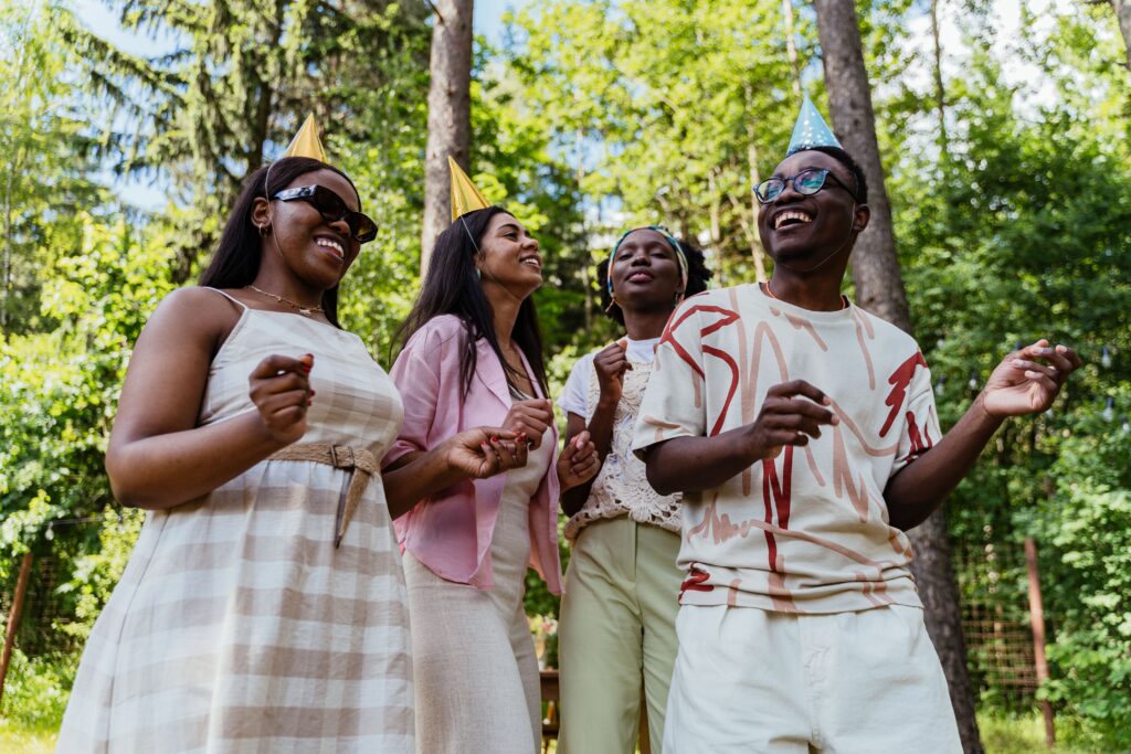 A group of diverse friends enjoying an outdoor party with party hats and smiles.