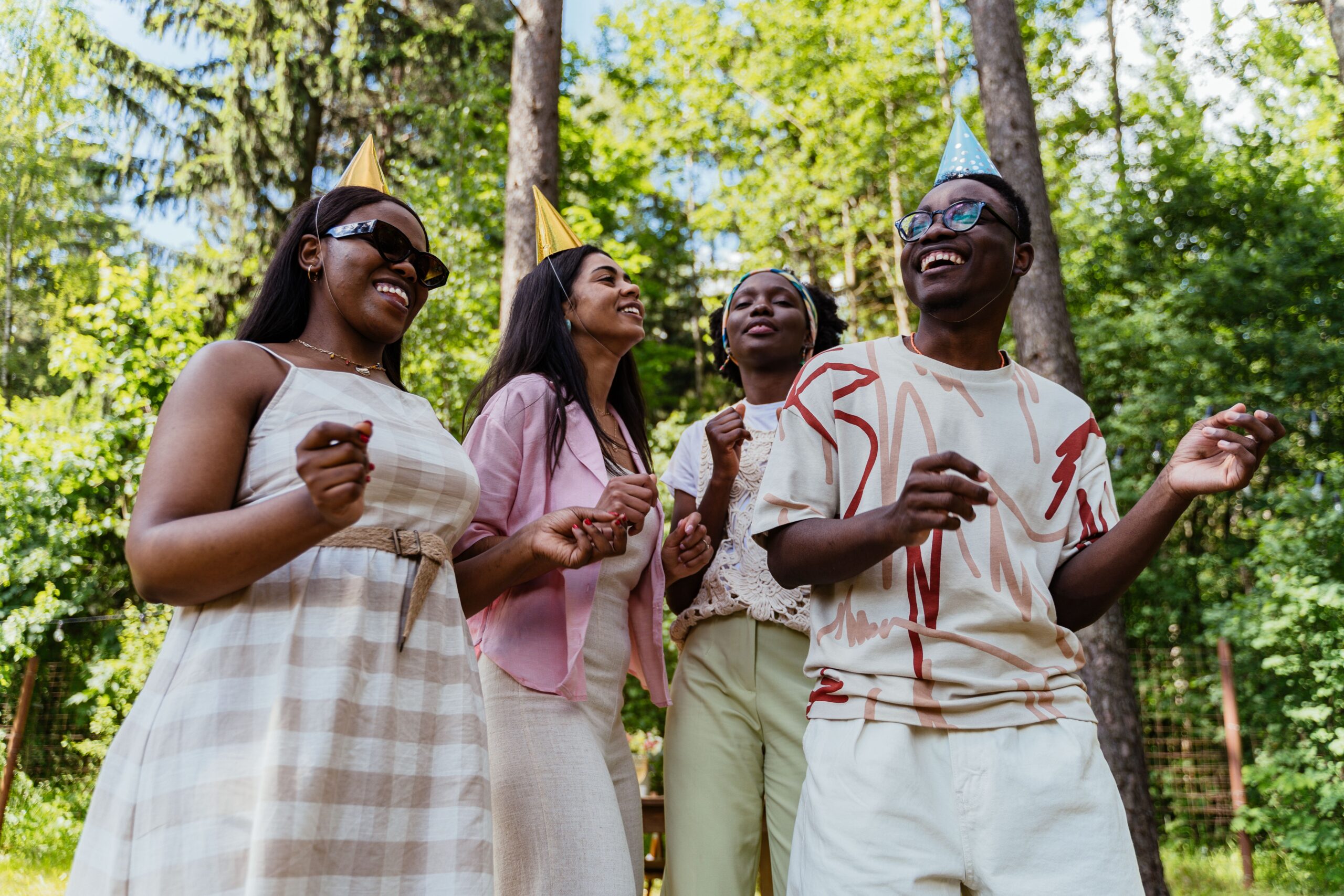 A group of diverse friends enjoying an outdoor party with party hats and smiles.